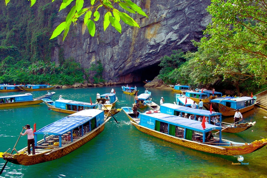 Wooden boats entering Phong Nha Cave surrounded by limestone cliffs – Auasia Travel